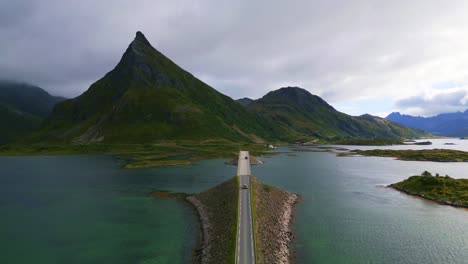 Following-cars-driving-along-the-Fredvang-bridge-in-Lofoten-Northern-Norway-with-the-sea-ocean-water-shimmering-in-light-turquoise-blue-and-green-tones-in-summer-with-view-to-the-mountains