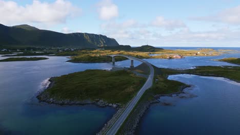 Aerial-shot-along-the-Fredvang-bridge-in-Lofoten-Northern-Norway-with-the-sea-ocean-water-shimmering-in-light-turquoise-blue-and-green-tones-on-a-sunny-day-in-summer