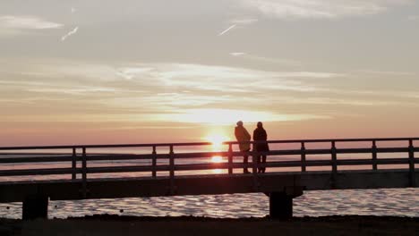 Two-Women-wath-sunset-on-elevated-bridge-at-the-North-Sea-while-low-tide