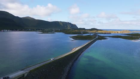 Siguiendo-El-Puente-Fredvang-En-Lofoten,-En-El-Norte-De-Noruega,-Con-Los-Coches-Circulando-Por-él-Y-El-Agua-Del-Mar-Que-Brilla-En-Tonos-Azul-Turquesa-Claro-Y-Verde-En-Un-Día-Soleado-De-Verano