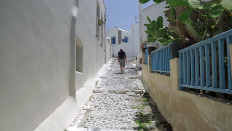 Following-a-man-walking-down-a-narrow-street-of-a-Greek-island-on-a-sunny-day