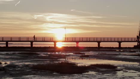 Person-walks-on-a-small-bridge-in-front-of-an-old-antique-lighthouse-while-sunset