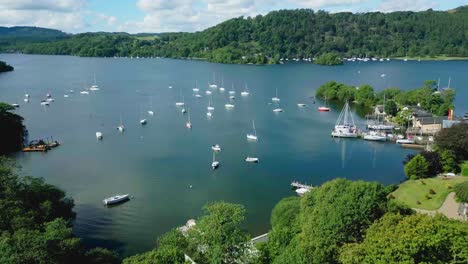 Colourful-Aerial-Drone-View-Over-Boats-And-Yachts-On-Lake-Windermere-At-Bowness-Marina-With-Hills-And-Trees-On-A-Sunny-Summer-Morning-With-Blue-Sky-And-Clouds