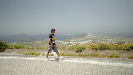 One-man-holding-a-camera-walks-on-a-high-point-of-Santorini-island-in-Greece
