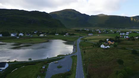 Flying-downwards-towards-street-road-in-Lofoten,-Norway-with-surrounding-fairytale-mountain-and-green-grass-landscape-with-tiny-houses-along-the-road