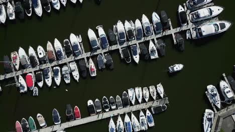 Rotating-Colourful-Aerial-Drone-View-Over-Boat-Moorings-And-Yachts-On-Lake-Windermere-At-Bowness-Marina-With-Small-Boat-Moving-Through-The-Scene-On-Sunny-Summer-Morning