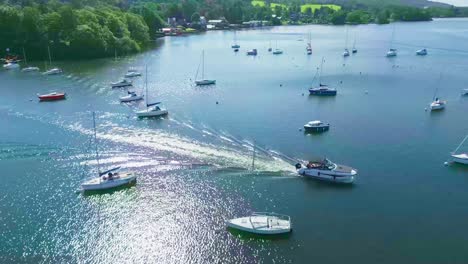 Elevated-Rotating-Aerial-Drone-View-Following-Small-Cruiser-Boat-On-Lake-Windermere-At-Bowness-Marina-With-Yachts-Throughout-The-Scene-On-A-Sunny-Summer-Morning-Showing-Algae-Problem-On-The-Lake