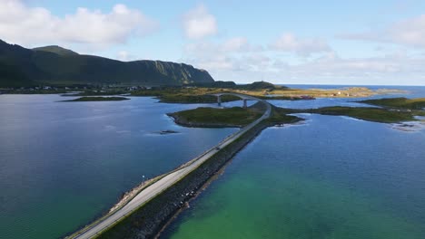 Following-a-car-driving-across-the-Fredvang-bridge-in-Lofoten-Northern-Norway-with-the-sea-ocean-water-shimmering-in-light-turquoise-blue-and-green-tones-on-a-sunny-day-in-summer