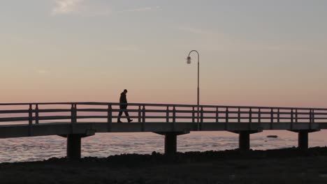 Man-walks-on-a-bridge-to-an-old-antique-lighthouse-at-the-North-Sea-while-sunset