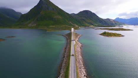Following-a-car-driving-along-the-Fredvang-bridge-in-Lofoten-Northern-Norway-with-the-sea-ocean-water-shimmering-in-light-turquoise-blue-and-green-tones-on-an-overcast-day-in-summer