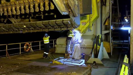 Hand-held-shot-of-a-worker-welding-metal-components-together-at-night-on-a-dredge