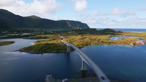 Following-a-black-car-driving-along-the-Fredvang-bridge-in-Lofoten-Northern-Norway-with-the-sea-ocean-water-shimmering-in-light-turquoise-blue-and-green-tones-on-a-cloudy-day-in-summer