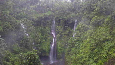 Aerial-flies-through-jungle-valley-mist-toward-multi-cascade-waterfall