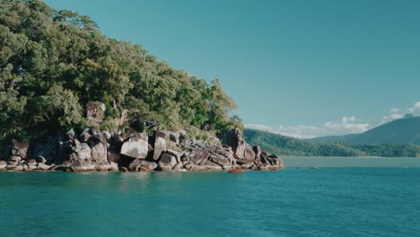 Tropical-rocky-island-with-trees,-tracking-shot-from-boat