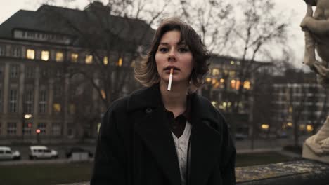 Young-woman-in-a-black-coat-standing-on-a-terrace-and-smoke