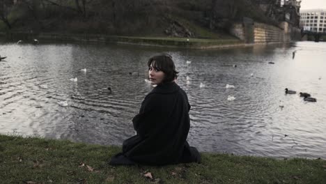 Young-woman-in-a-black-coat-sitting-in-a-park-in-autumn-in-afternoon-and-feeding-ducks-in-a-sea-4