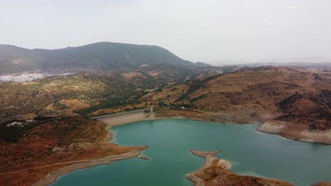 Aerial-approach-to-hydraulic-dam-blue-lake-surrounded-by-dry-grass-and-mountains