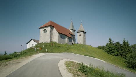 Toma-Constante-De-La-Antigua-Iglesia-En-La-Cima-De-La-Colina-Cerca-De-La-Ruta-Y-El-Bosque,-Kum-Eslovenia