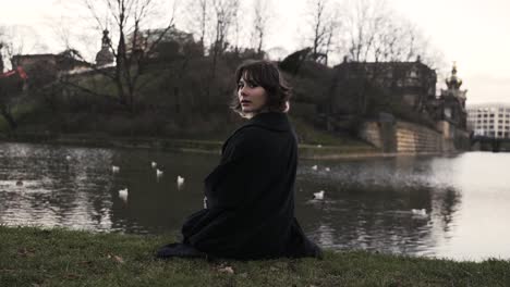Young-woman-in-a-black-coat-sitting-in-a-park-in-autumn-in-afternoon-and-feeding-ducks-in-a-sea-3