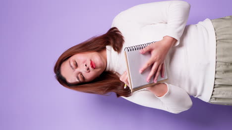 Vertical-of-Asian-secretary-businesswoman-holding-a-notebook-and-thinking-with-list-inspiration-strategy-for-success-on-purple-background-1