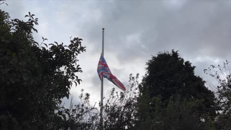 Union-Jack-flag-of-Great-Britain-flutters-at-half-mast-between-trees