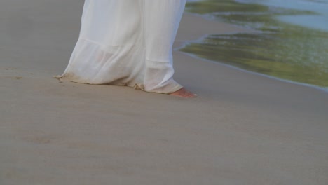 Füße,-Die-Im-Sand-Am-Strand-Spazieren-Gehen,-Bevor-Die-Aufsteigende-Kamera-Eine-Junge-Frau-In-Einem-Strandkleid-An-Einem-Sonnigen-Tag-Am-Strand-Zeigt