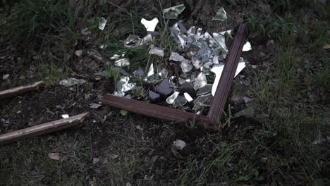 Slow-motion-shot-of-shards-of-glass-from-a-broken,-shattered-mirror-laying-on-the-ground-in-the-grass