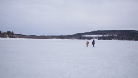 Panning-shot-across-Holiday-Club-Katinkulta,-Vuokatti,-Finland-hikers-standing-on-frozen-woodland-lake