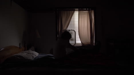 Silhouette-of-a-young-high-school-aged-teen-boy-sits-up-on-his-bed-at-night