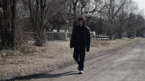 A-young-high-school-aged-teen-boy-wearing-a-backpack-walking-down-a-road-during-the-winter-on-a-cold-day