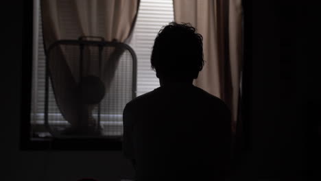Silhouette-of-a-young-high-school-aged-teen-boy-sitting-on-his-bed-in-his-bedroom