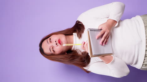 Vertical-of-Asian-secretary-businesswoman-holding-a-notebook-and-thinking-with-list-inspiration-strategy-for-success-on-purple-background-2