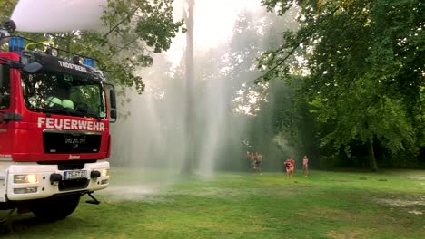 Deutsches-Feuerwehrauto,-Das-An-Einem-Heißen-Sommertag-Wasser-Für-Kinder-Und-Bäume-Sprüht-10
