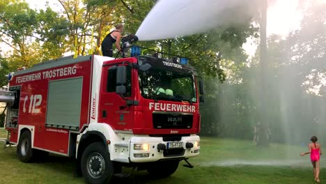 Deutsches-Feuerwehrauto,-Das-An-Einem-Heißen-Sommertag-Wasser-Für-Kinder-Und-Bäume-Sprüht-8