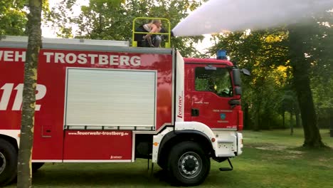 Deutsches-Feuerwehrauto,-Das-An-Einem-Heißen-Sommertag-Wasser-Für-Kinder-Und-Bäume-Sprüht