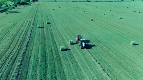 Tractor-baling-round-bales-in-Bulgaria,-july-2018,-drone-filming-around-it