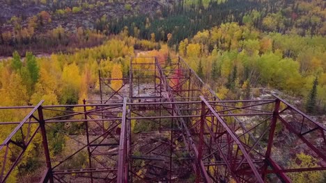 Fly-over-shot-of-an-abandoned-mine-building-frame-in-the-boreal-forest-in-the-fall-with-a-lake-in-the-background