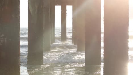 Slow-tilt-into-the-sunlight-under-a-beach-pier