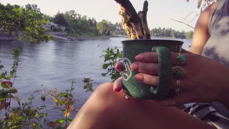 Cute-hipster-girl-relaxing-by-a-river-or-lake-with-a-mug