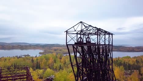 Slow-motion-Aerial-Orbit-Panning-shot-of-an-abandoned-mine-headframe-in-the-boreal-forest-in-the-fall-with-a-lake-in-the-background