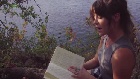 Cute-hipster-girl-reading-a-book-out-loud-to-the-camera-in-a-local-park-by-a-river