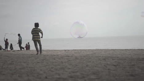 Eine-Blase,-Die-Vor-Der-Kamera-Fliegt,-Während-Die-Leute-Am-Strand-Spielen
