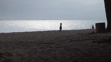 Silhouette-Eines-Kleinen-Kindes,-Das-Am-Strand-Mit-Sonnenlichtreflexions-Meereshintergrund-Läuft