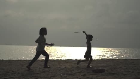 Silhouette-Von-Kindern,-Die-Bei-Sonnenuntergang-Am-Strand-Spielen-Und-Blasen-Jagen