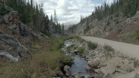 Dolly-shot-of-stream-next-to-dirt-road-in-the-mountains-of-Colorado-in-late-summer