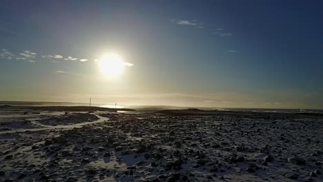 Vuelo-Aéreo-Moviéndose-Rápidamente-A-La-Costa-Sobre-Terreno-Rocoso-Nevado-En-Keflavik,-Islandia