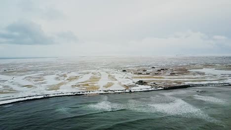 Aerial-shot-pulling-back-from-Sandgerdi-Iceland-with-small-cottages-dotting-the-coast-and-white-capped-waves-hitting-the-shore