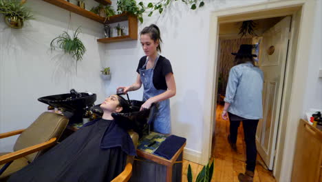Slow-mo-walking-through-hair-salon-with-a-hairdresser-washing-a-clients-hair-in-a-basin