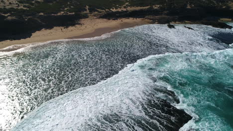 Drone-over-beach-as-the-waves-crash-up-against-the-shore-line-at-Pearses-Beach,-Victoria