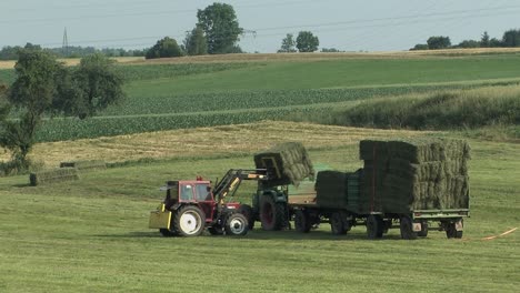 Hay-harvest-near-Neuburg-an-der-Donau-with-tractor-loading-hay-bale,-Bavaria,-Germany